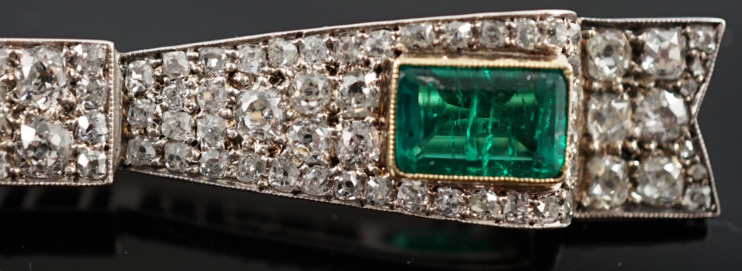 A 1920's gold and platinum, two stone emerald and graduated diamond cluster set ribbon bow bar clip brooch